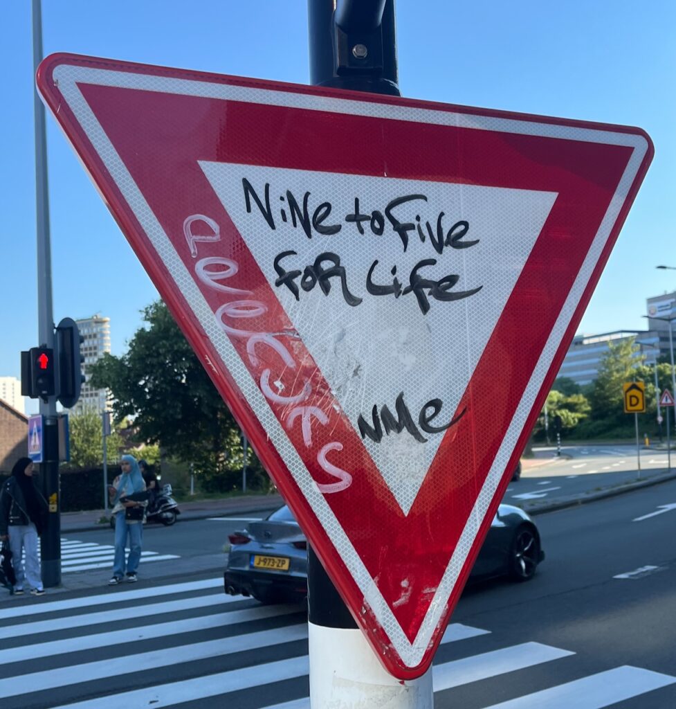A traffic sign. Someone wrote the words Nine to five for life on it.